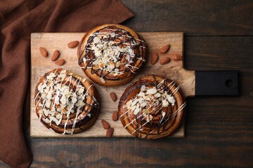 Delicious rolls with toppings and almonds on wooden table, top view. Sweet buns