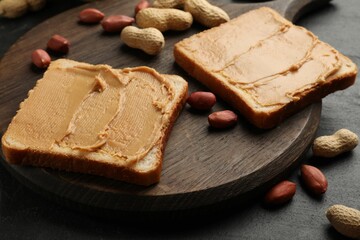 Tasty peanut butter sandwiches and peanuts on black table, closeup
