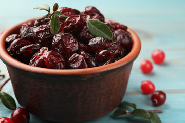 Tasty dried cranberries in bowl, fresh ones and leaves on table, closeup