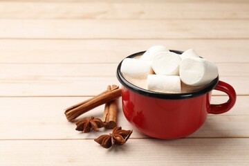 Tasty hot chocolate with marshmallows and spices on light wooden table, closeup. Space for text