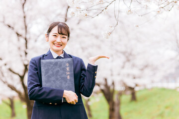 満開の桜の下で卒業証書を持つ高校生・女子高生（卒業生・卒業式・卒業・こちら・おすすめ・案内）
