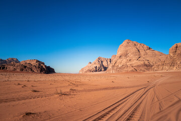 Fototapeta na wymiar Wadi Rum, Jordan, Scenic view of Arabic Middle Eastern desert against clear blue sky with sand tracks in foreground. Mountain in background. Copy space no people