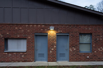 Brick building with flood light illuminated.  Two blue doors and a window on eaach side.