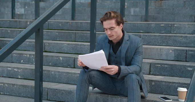 Businessman sitting on stairway diligently tackling paper work Concentration on paperwork reflects mind deeply engaged in brainstorming. Paperwork in his hands tells tale of bureaucracy and reports.