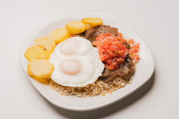 Authentic, traditional Bolivian meal: Silpancho, made of beef, potatoes, rice, fried eggs, tomato and onion salad. close-up on white plate on white background. copy space