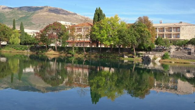 Picturesque mountain landscape of country village with stone houses, trees reflected in lake, car driving along deserted bridge Ecotourism excursion to mountain village, water retreat Cottage by river