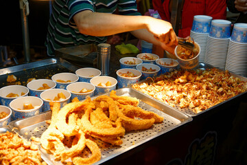 Fototapeta premium A stall vendor selling crispy fried seafood in paper cups, one of local people's favorite street-foods, in Flower Night Market, where many traditional snacks can be savored, in Tainan, Taiwan, Asia