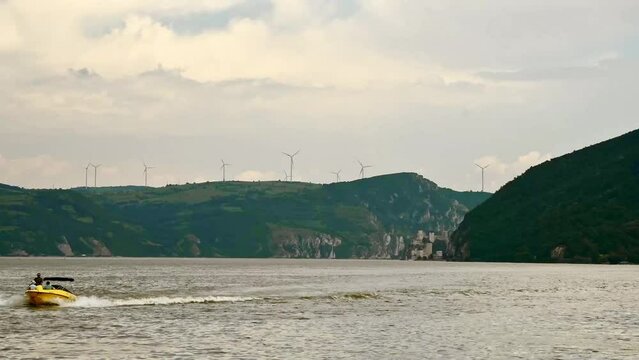 Time lapse of boat sailing on river and wind turbines in background on a hill