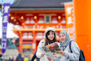 Travel, muslim, Two Asian female tourists of different religions friends visitor learning about history of fushimi inari shrine in travel book while walking through senbon torii path in Kyoto Japan.