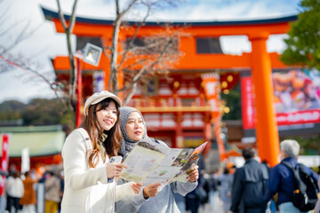 Travel, muslim, Two Asian female tourists of different religions friends visitor learning about history of fushimi inari shrine in travel book while walking through senbon torii path in Kyoto Japan.