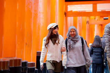 Travel, muslim, Two Asian female tourists of different religions friends visitor learning about history of fushimi inari shrine in travel book while walking through senbon torii path in Kyoto Japan.