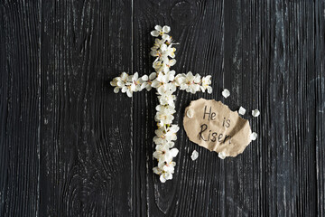 Cross with flowers on a wooden background with the inscription Christ is Risen. Easter concept. Cross symbolizing the death and resurrection of Jesus Christ
