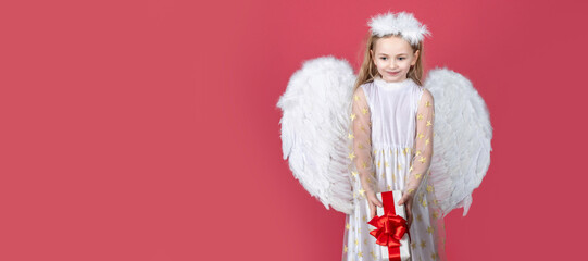 Angel child banner, isolated studio background. Kid girl angel with present gift, studio portrait. Little angel with white wings holds gift. Cute angel child girl with angels wings, isolated on red.