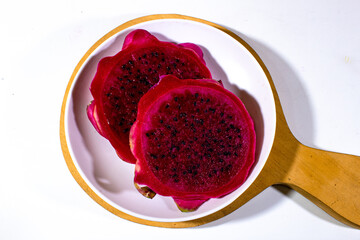 Several pieces of red dragon fruit are served on a white plastic plate and on a wooden coaster