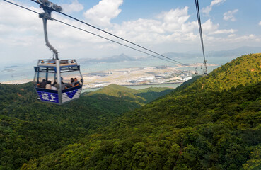 Tourists ride in a gondola of Ngong Ping Cable Car (Skyrail) gliding over the mountainside & enjoy the panoramic view of Hong Kong International Airport on Chek Lap Kok Island in Hongkong, China, Asia