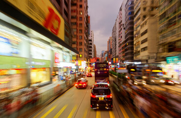 Night scape of trolley cars and double-decker buses dashing on a busy street flanked by office towers and colorful neon signs, in vibrant Mong Kok commercial district, in Kowloon Downtown, Hong Kong