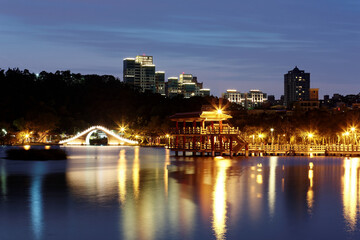 Fototapeta na wymiar A beautiful corner of Dahu Community Park with a traditional arch bridge and an oriental pavilion by lakeside in Taipei City, Taiwan ~ Night scene of an urban park with lights reflecting on lake water