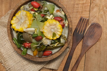 Sayur lodeh or vegetables with coconut milk soup is traditional Indonesian culinary food from Java in white bowl served on coconut tree trunk bowl, on a wooden table. Selective focus. Top view. 
