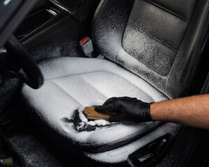 Man cleaning black leather car seat with brush and cleaning foam. 