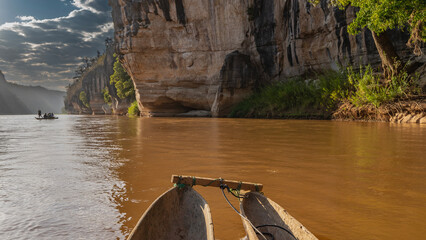 Wooden traditional canoes with tourists sail along the calm red-brown river. Glare on the water....