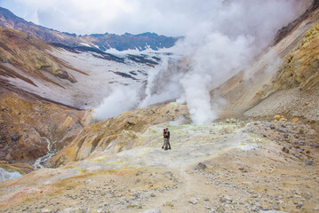 There are man and woman on the foreground. It is Mutnovskiy voclano. There is a field of fumaroles on the background.