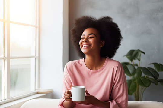 Happy African American Woman Enjoying Quiet Time At Home Laughing, Drinking Morning Coffee Sitting On Sofa. Copy Space.