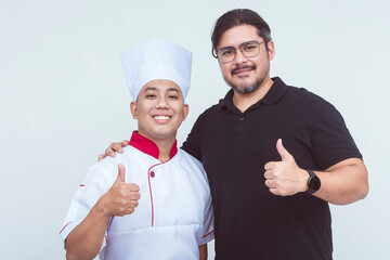 An asian chef together with his boss, the restaurant owner, making thumbs up signs. Isolated on a white background.