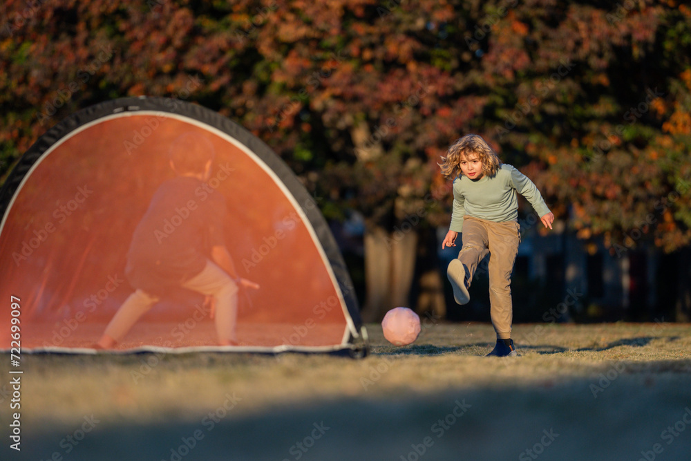 Wall mural Child boy football or soccer player in action on football stadium kicking football ball for goal. Concept of sport, competition. Kid kick football ball. Kid kicking soccer ball. Sport for kids.