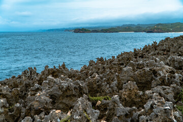 Hills full of sharp coral rocks that directly border the blue sea with a small island in the middle of the sea. Coral hills on the beach with a very beautiful blue sea in the background