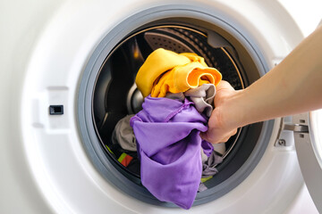 A woman opens the front door of a washing machine and puts clothes into the washing machine to...
