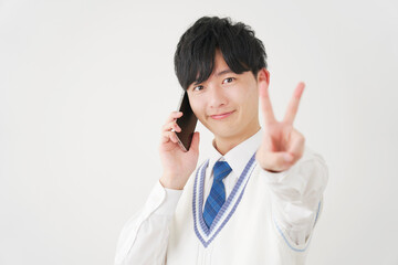 スマートフォンで電話しながらピースサインをする男子高校生　白背景