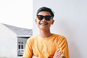 Stylish young guy hipster wear braces teeth and sunglasses standing in crossed arm with happy expression - obrazy, fototapety, plakaty