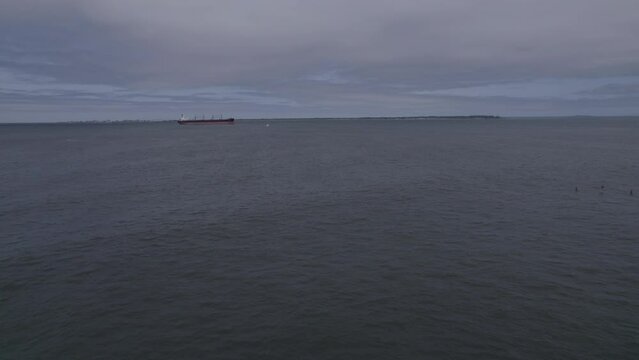 Ungraded drone footage depicts the vast, tranquil waters of Washington with a lone cargo ship traversing the horizon, a testament to the state’s thriving maritime routes.