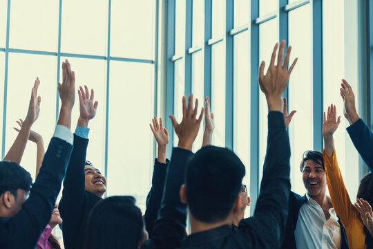 Successful business people raised their hands up for voting showing their approval volunteering in the office seminar with happiness. Smile managers put their hands up in the air. Intellectual.