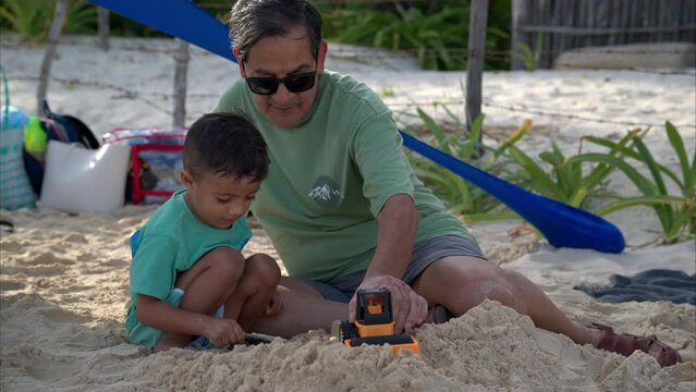 Slow motion of a latin toddler with his grandfather playing on the beach with the sand and some toys