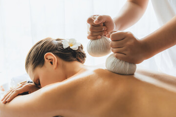 Hot herbal ball spa massage body treatment, masseur gently compresses herb bag on woman body....