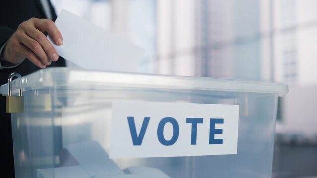 Close Up on Hands of an Anonymous Female and Male Voters Casting Their Votes and Putting Ballots into a Sealed Box. People Visiting a Polling Station on Elections Day in a Generic No Logo Setting