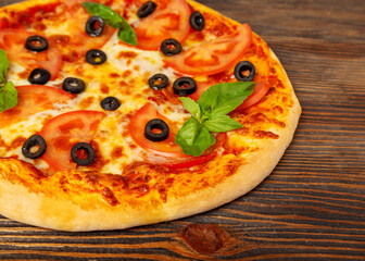 Pizza with tomato, mozzarella, olives and basil on a wooden background, close-up