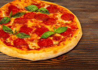 Pepperoni pizza with basil on wooden background, close-up