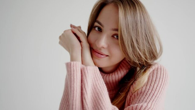 Blonde woman skillfully changes facial expressions from happiness to severity. Smiling young actress presses hands to cheek against gray background to take photo. Photographic session