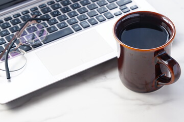 コーヒーを飲みながらノートパソコンでデスクワークをしているイメージ
