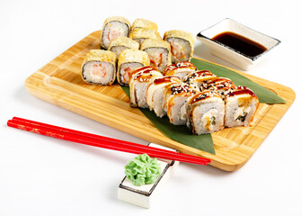 Assorted Japanese sushi roll with soy sauce on a wooden board, isolated.