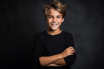 Fototapeta na wymiar Portrait of a happy young boy on a dark background with arms crossed