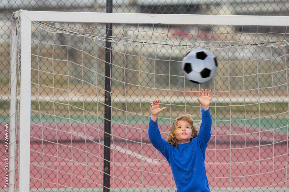 Wall mural Child boy football or soccer player in action on soccer stadium kicking soccer ball for goal. Concept of sport, competition. Kid kick soccer ball. Kid kicking football ball. Sport for kids.