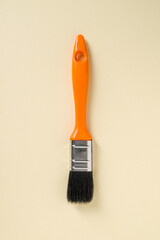 Touch-up paint brush with orange handle on yellow background