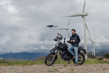 Motorcyclist operating drone. Wind turbines in the mountains.