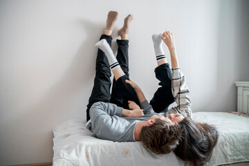 A young couple enjoys a relaxed, affectionate moment together while lying on a bed, with their legs...