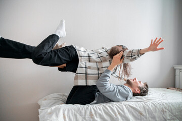 A joyful couple engages in a lighthearted and playful activity on a cozy bed in a well-lit room,...