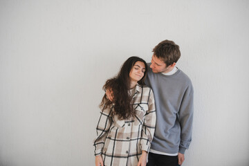 A young couple stands close together in an embrace, expressing affection and comfort in a minimalistic indoor environment.