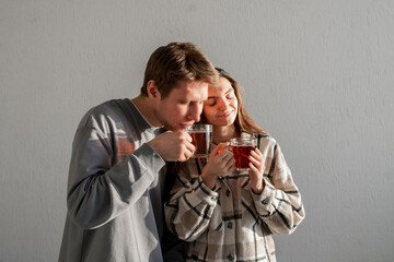 A young couple stands close, enjoying the comforting aroma and taste of tea, sharing a tranquil...